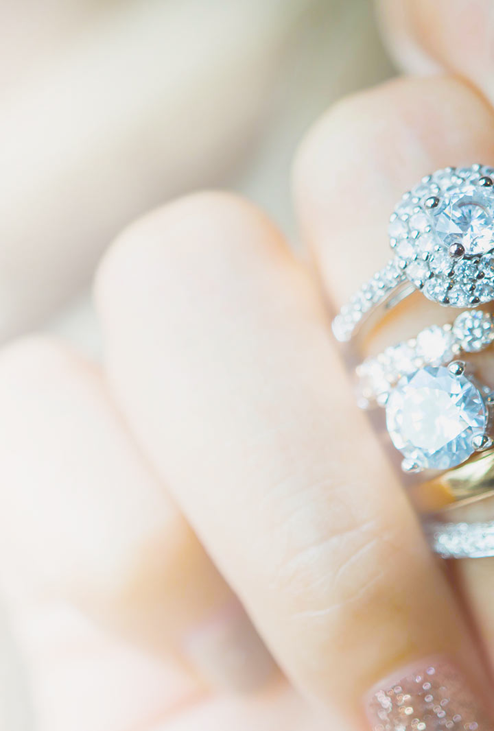 the edge of a stack of various style diamond rings displayed on a female hand
